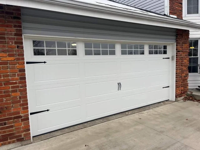 A white Garage Door with black decorative handles and hinges is attached to a brick house in West County St. Louis. A white Garage Door with black decorative handles and hinges is attached to a brick house in West County St. Louis.